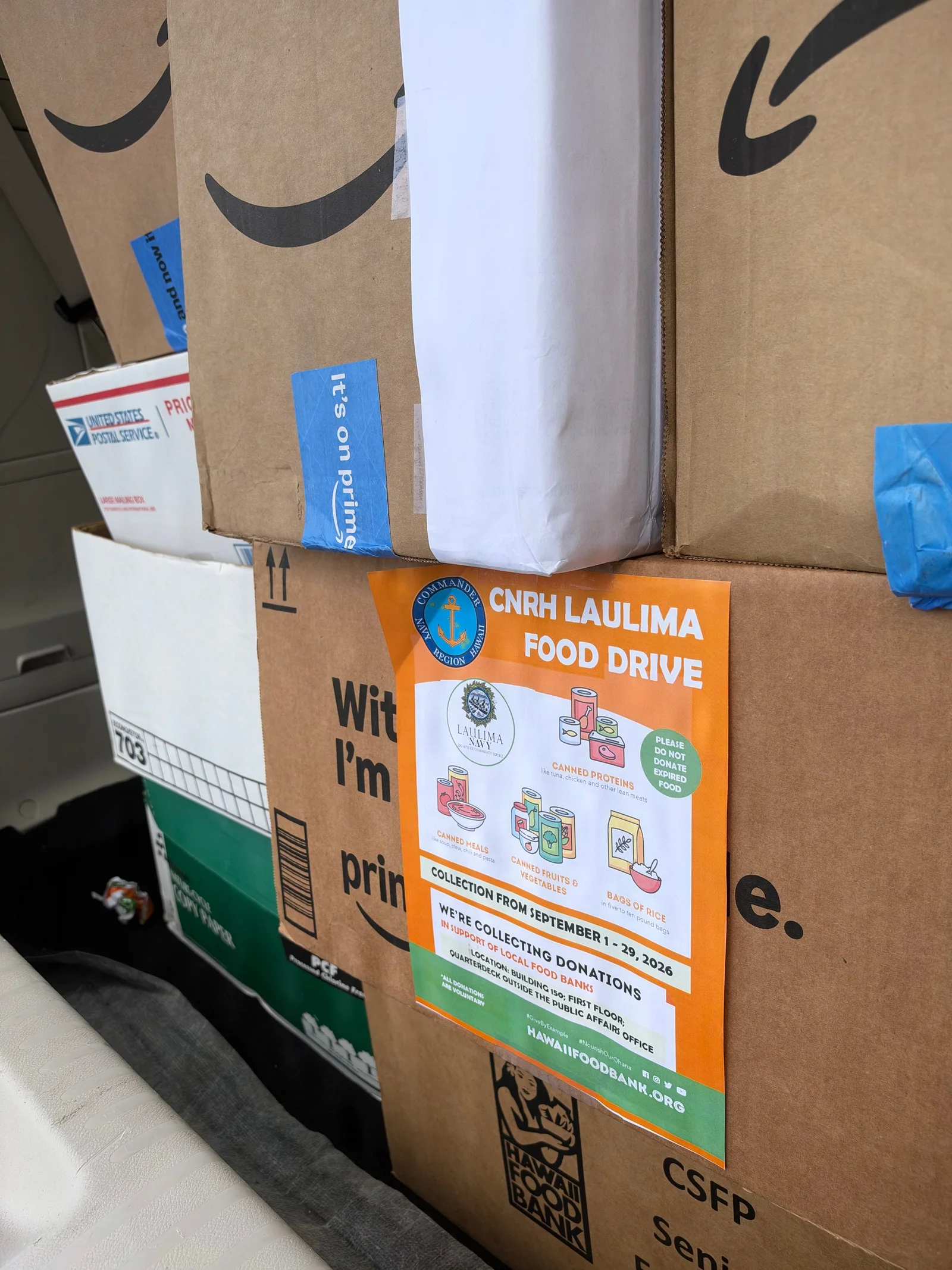 Stacked donation boxes display a colorful Navy Region Hawaii food drive sign